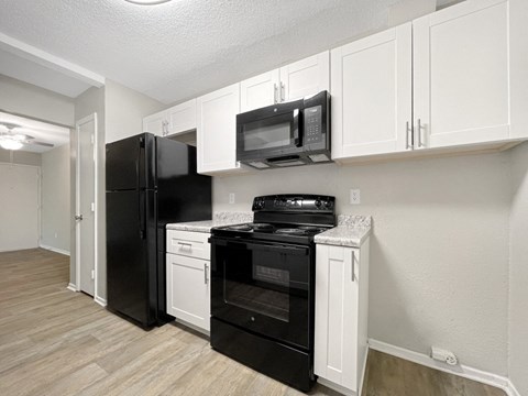 A black refrigerator and oven in a kitchen with white cabinets.