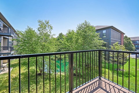 A balcony with a black railing overlooks a green lawn and trees.