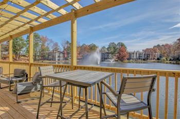 a patio with a table and chairs overlooks a lake with a fountain