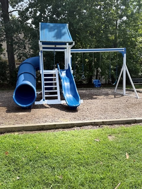 A blue slide and chair are in the foreground of a playground.