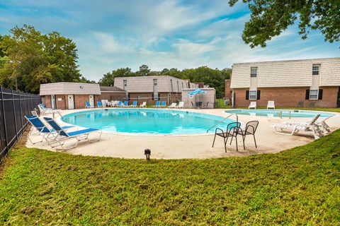 A pool surrounded by lawn chairs and trees.