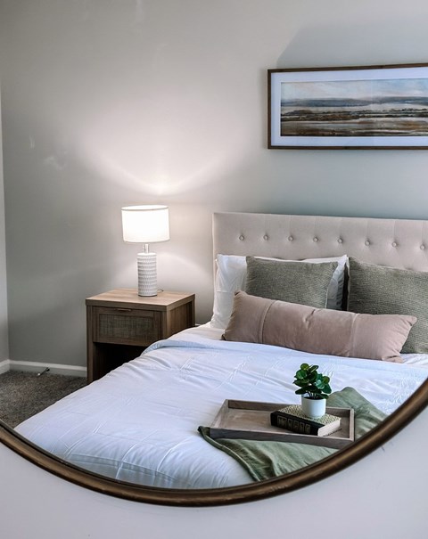 A bedroom with a bed, a nightstand with a lamp, and a painting on the wall.