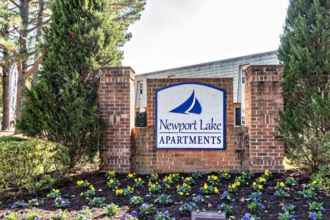 A sign for Newport Lake Apartments is displayed on a brick wall.