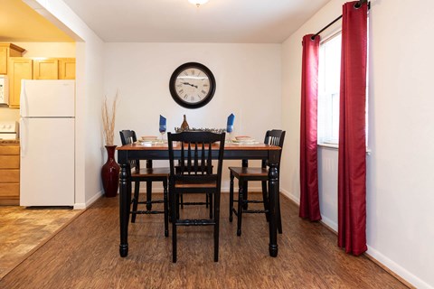 A dining room with a table and chairs and a clock on the wall.