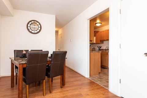 A dining room with a table and chairs and a clock on the wall.