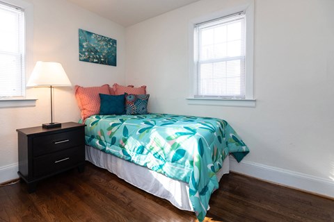 A bedroom with a bed, a nightstand with a lamp, and a painting on the wall.