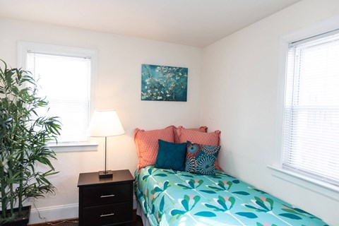 A bedroom with a bed, nightstand, and a potted plant.