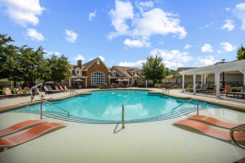 A large swimming pool with lounge chairs and a house in the background.