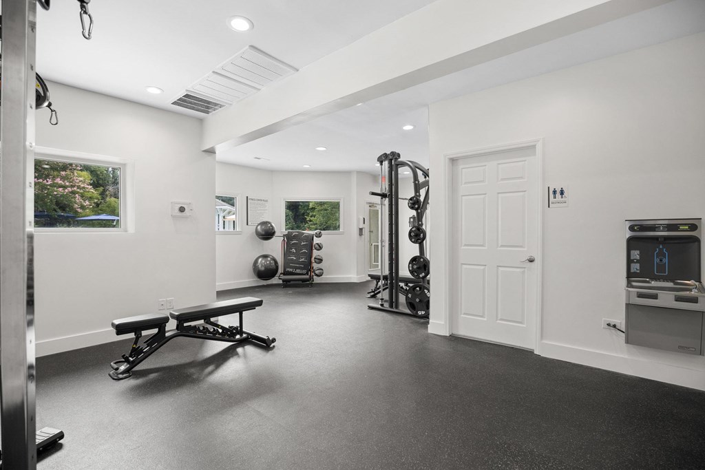 A black and white photo of a home gym with a bench, weights, and exercise equipment.