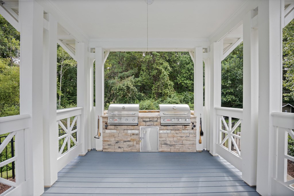 A white gazebo with a stone wall and grill in the middle.