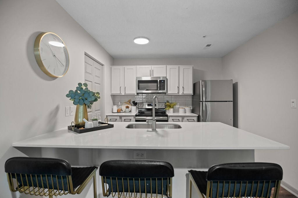 A kitchen with a white countertop and black chairs.