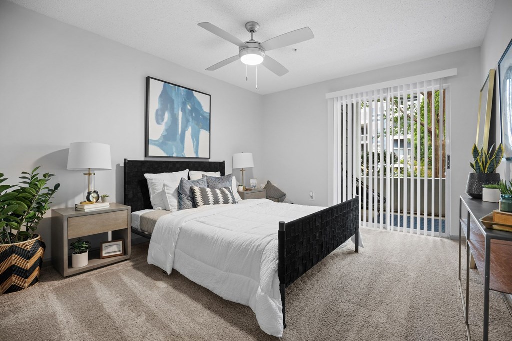 A bedroom with a large bed, a ceiling fan, and a painting on the wall.