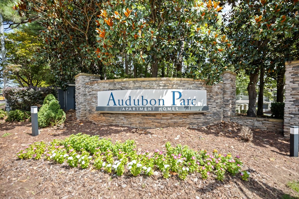 A sign for Audubon Park in front of some trees.
