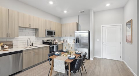 A kitchen with a table set for two with a refrigerator and microwave above.