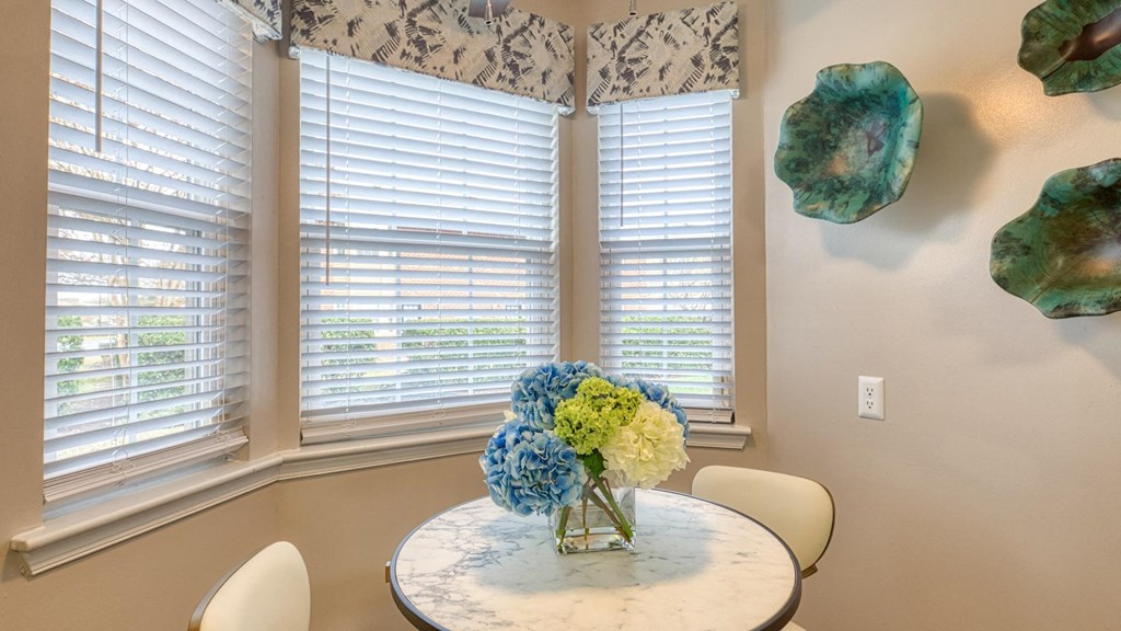 A dining room with a table and chairs and a vase of flowers.