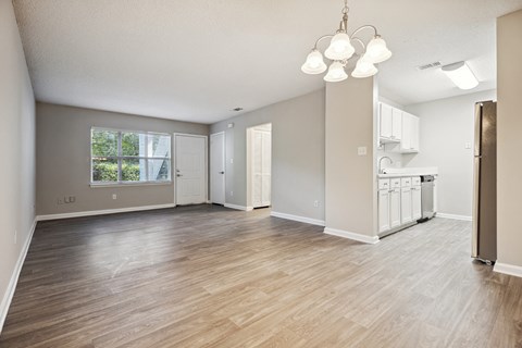 an empty living room with a kitchen in the background