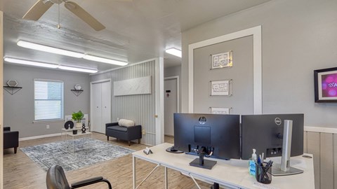 A room with a desk, chairs, and a ceiling fan.