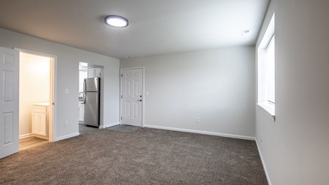 an empty living room with white walls and a door to the kitchen