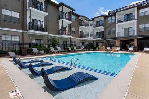A swimming pool with lounge chairs in front of apartment buildings.