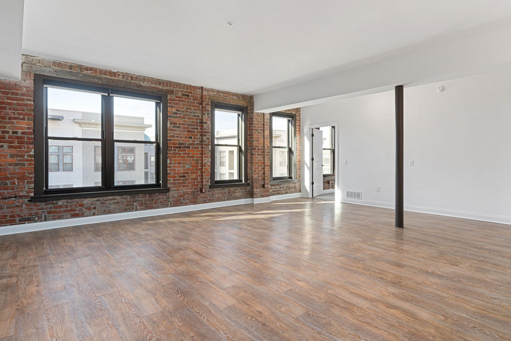 an empty living room with a brick wall and wood floors at The Madison, Columbus