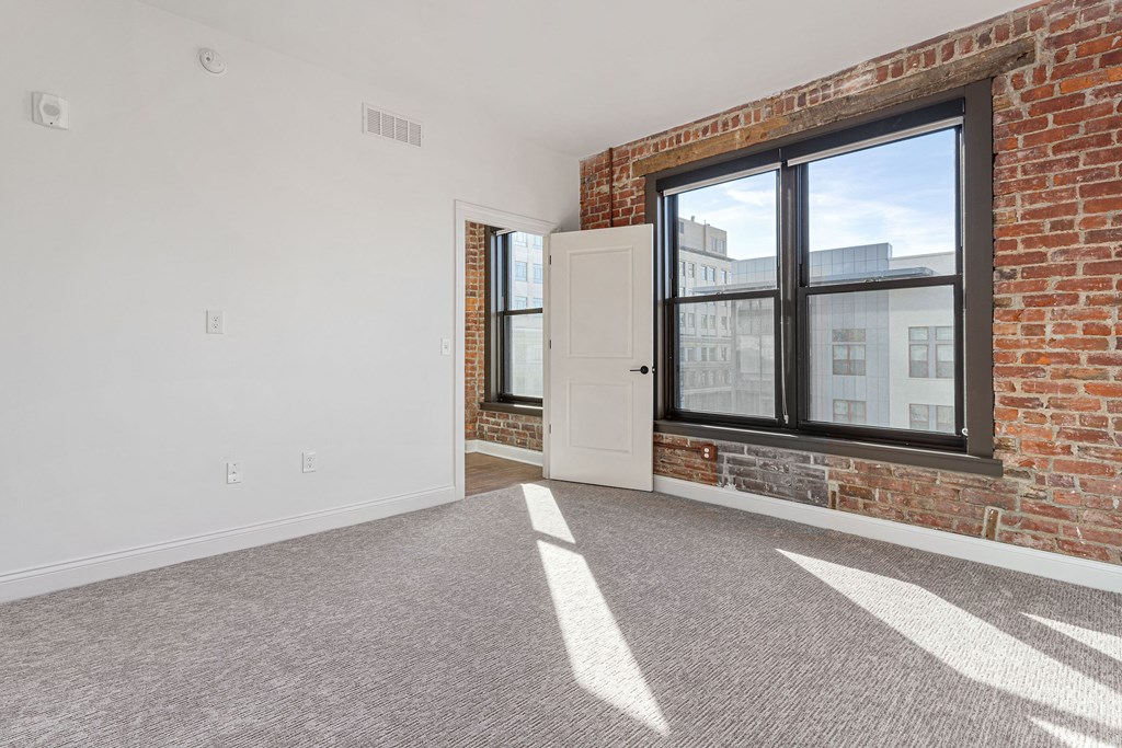 an empty living room with a brick wall and a large window at The Madison, Columbus, 43215