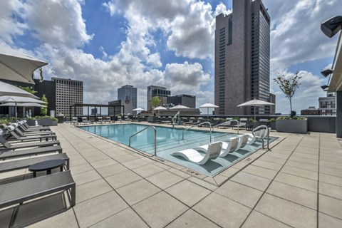 A pool surrounded by chairs and umbrellas with a city skyline in the background.