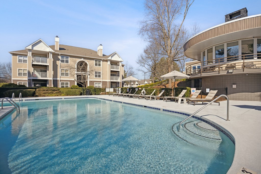 a large pool with chairs and a building in the background