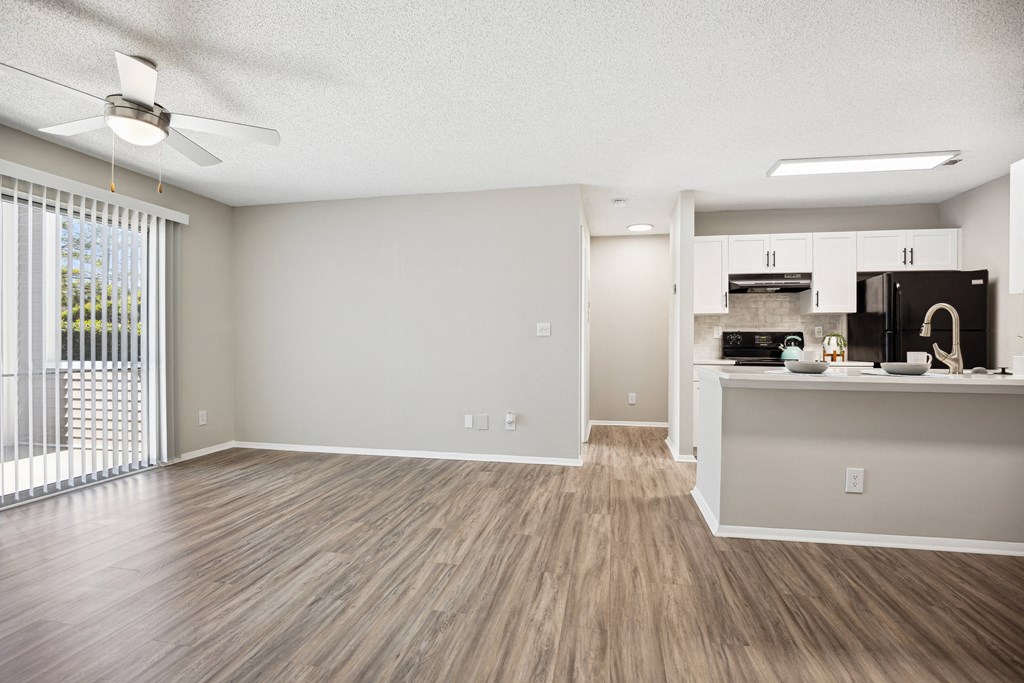 an empty living room with a kitchen and a window