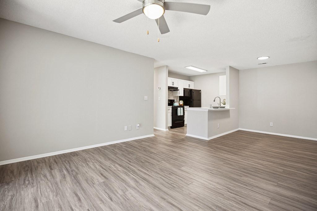 an empty living room with a ceiling fan and a kitchen
