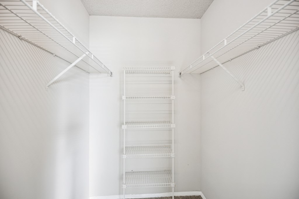 a walk in closet with white walls and white shelves and a ladder on the wall