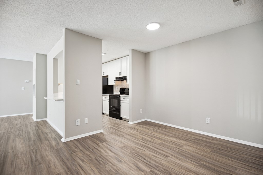 an empty living room and kitchen with white walls and wood flooring