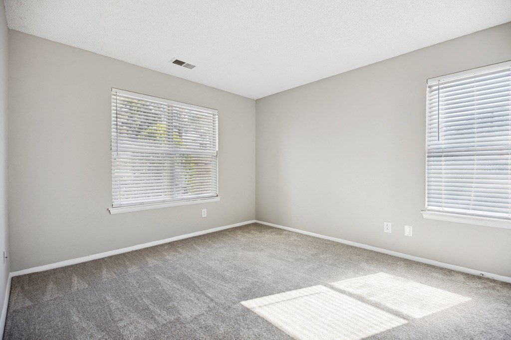 an empty room with carpet and two windows
