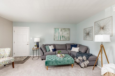 A living room with a grey couch, a green ottoman, and a painting on the wall.