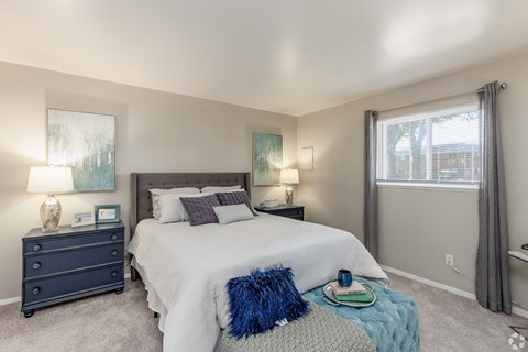 A bedroom with a large bed, a nightstand with a lamp, and a window with curtains.