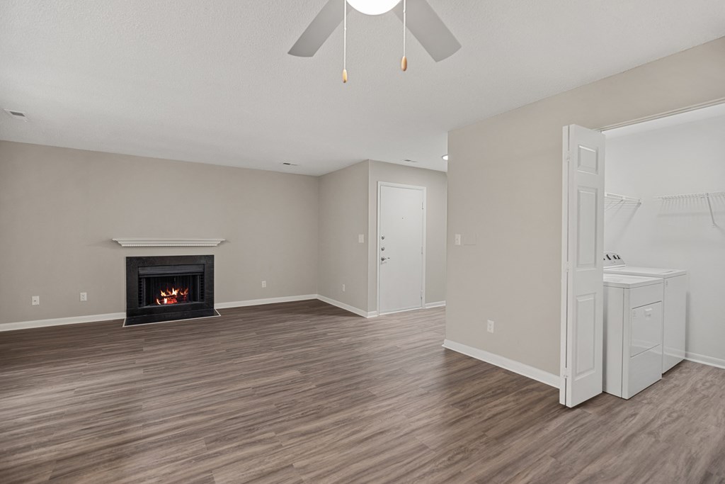 an empty living room with a fireplace and a white kitchen
