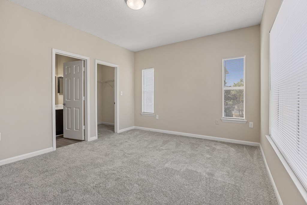 an empty living room with white blinds and a door to a bathroom