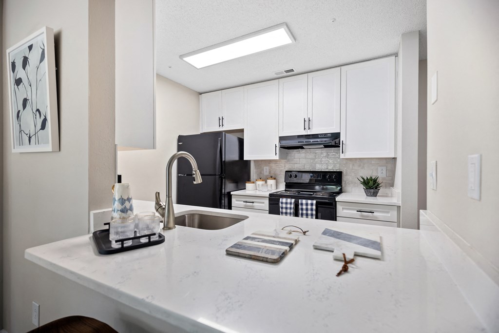 an open kitchen with white cabinets and a white counter top with a sink and stove