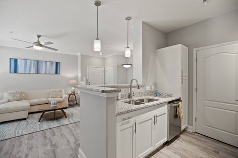 A modern kitchen with a white color scheme and a living room area with a sofa and a table.