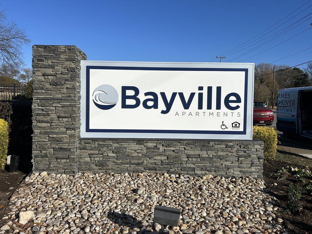 A property sign for Bayville Apartments is displayed in front of a stone wall.