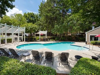a swimming pool with chairs around it and trees in the background