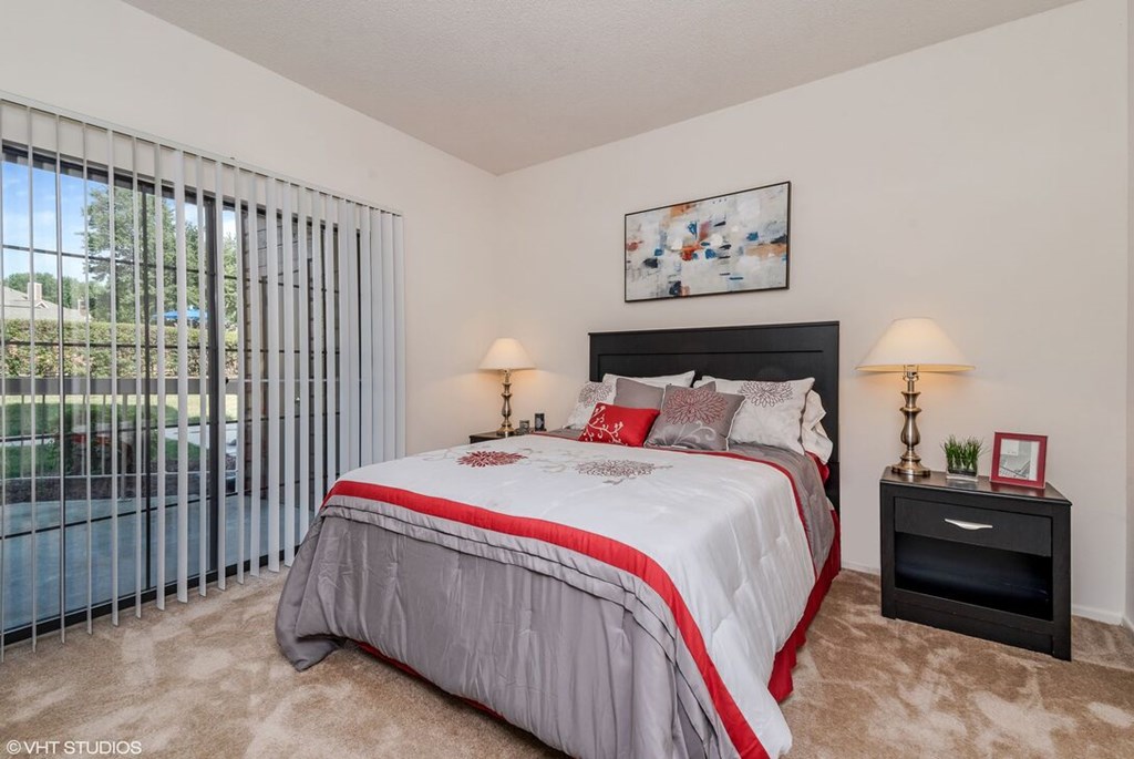 A bedroom with a large bed and a window with blinds.