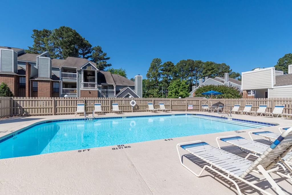 A swimming pool surrounded by lounge chairs and buildings in the background.
