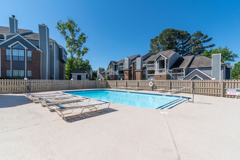 A swimming pool surrounded by a fence and lounge chairs.