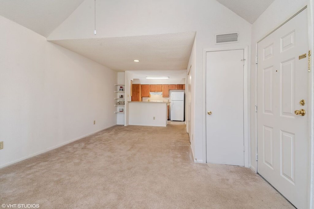A white room with a door on the right and a kitchen area visible through the door.