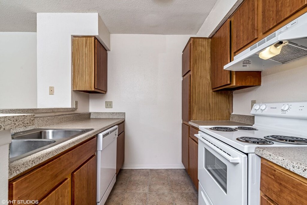 A kitchen with a white stove top oven and wooden cabinets.