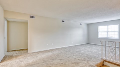 A spacious room with a carpeted floor and a window with white blinds.