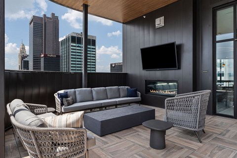 A modern balcony with a grey sofa, wicker chair, and a television.