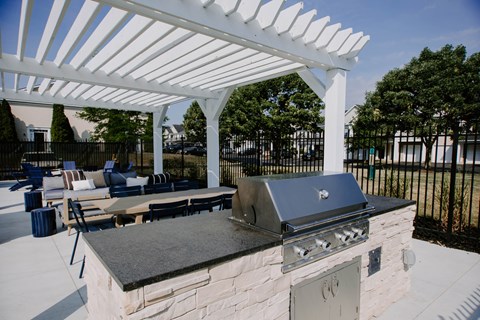 A white pergola is over a stone and metal grill.