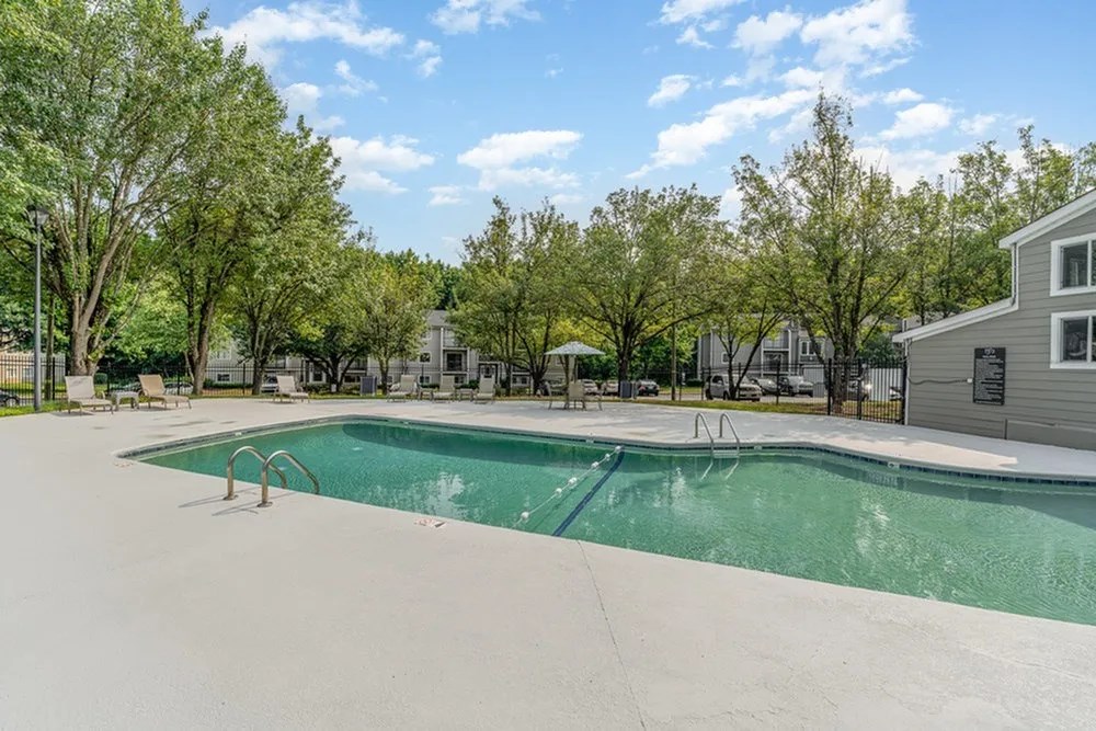 a swimming pool with trees and buildings in the background at Village 1373, Greensboro, NC