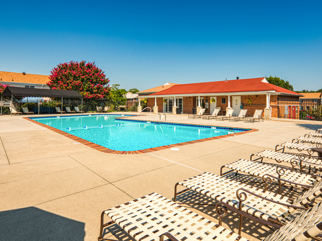 A pool with sun loungers and a building in the background.